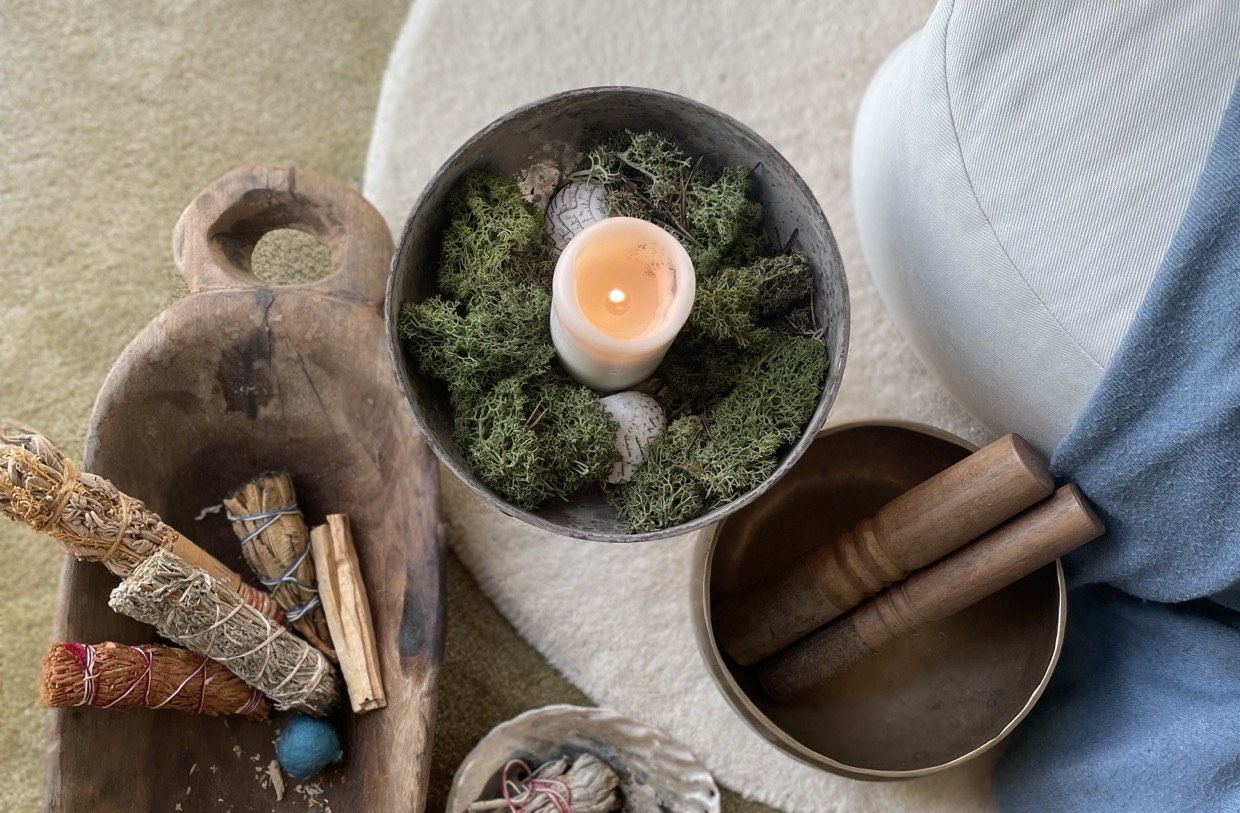 A smudge bundle in a wooden bowl, a candle set in moss and a singing bowl with strikers